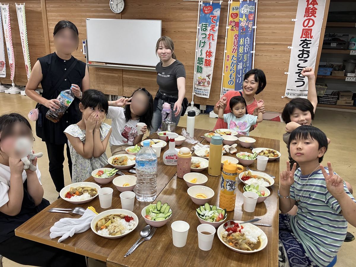 修学旅行先の食堂で、自分たちでつくったカレーを囲む小中学生とスタッフの集合写真。岡山県の体験施設にて