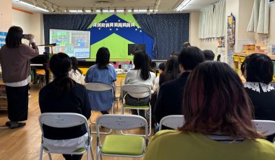 2026年3月21日の卒業式＆修了パーティ、巣鴨の現地会場で生徒・保護者・スタッフがふりかえりアルバムの上映を見ている様子