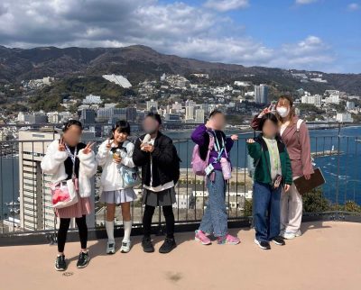 熱海城の展望台で海と街をバックにVサインで並ぶaini schoolの生徒たちとスタッフ