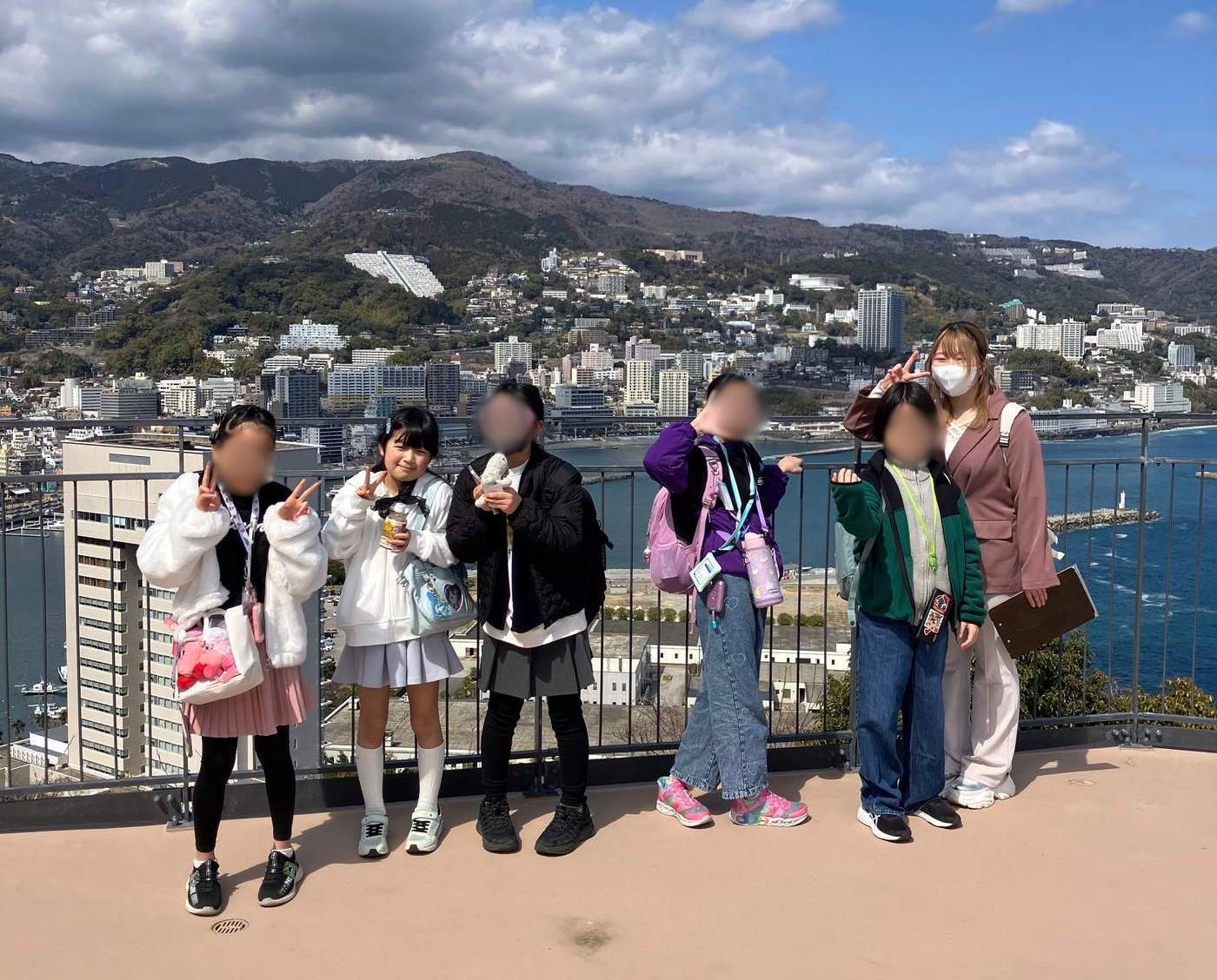 熱海城の展望台で海と街をバックにVサインで並ぶaini schoolの生徒たちとスタッフ