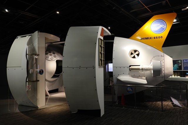 三菱みなとみらい技術館に展示された深海調査船しんかい6500の実物大模型。暗い展示室の中で存在感を放つ白い船体