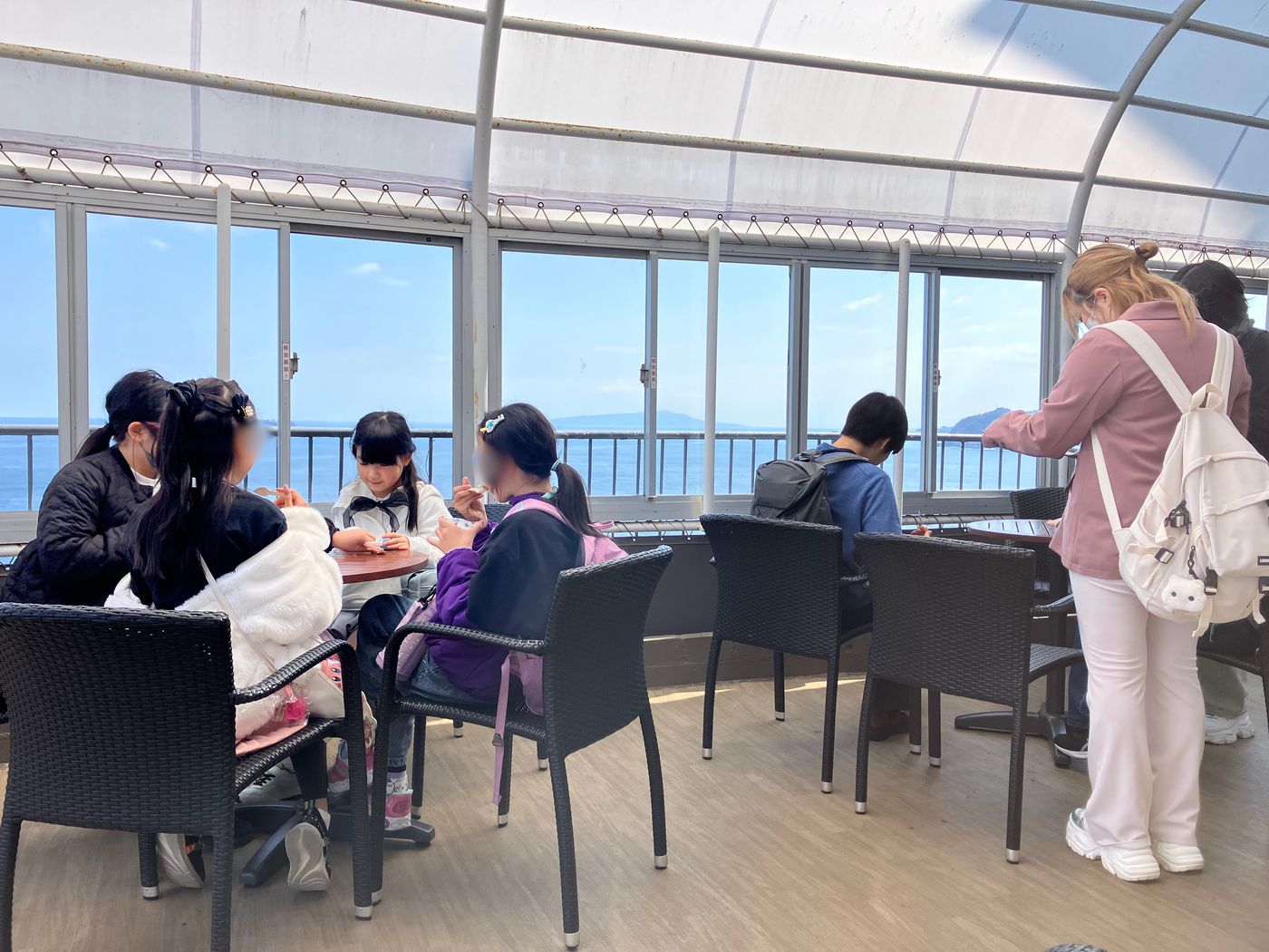 海が一望できるテラス席でお昼ごはんを食べるaini schoolの生徒たち。窓の外に相模湾が広がる