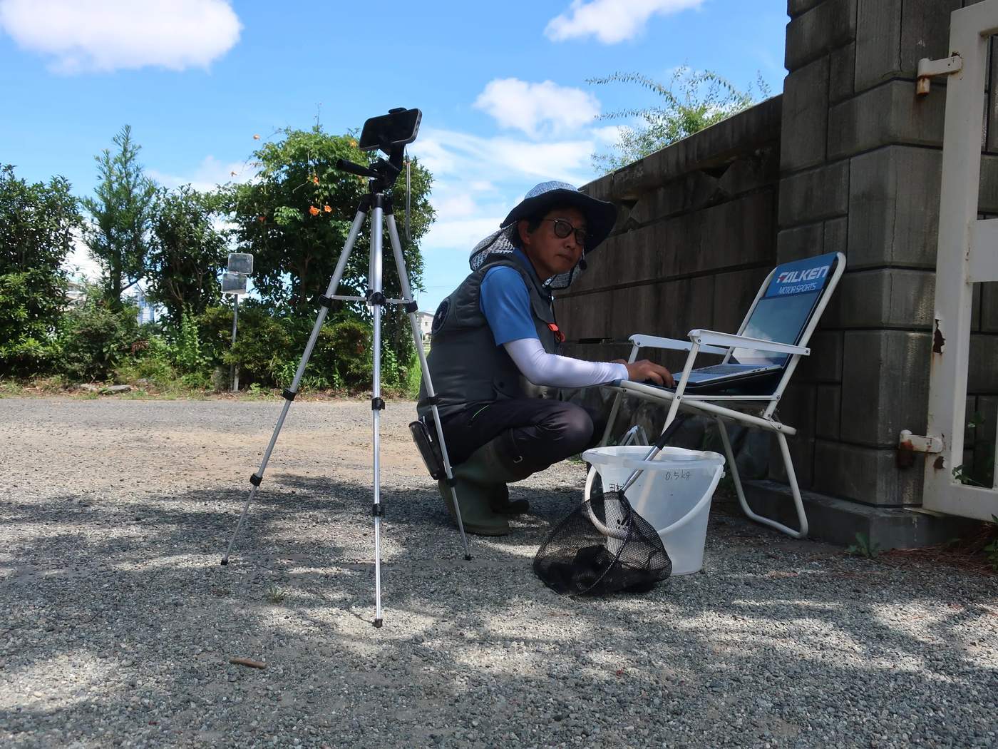 田んぼのそばで三脚とパソコンをセットし、オンライン授業の配信準備をするタムライスさん