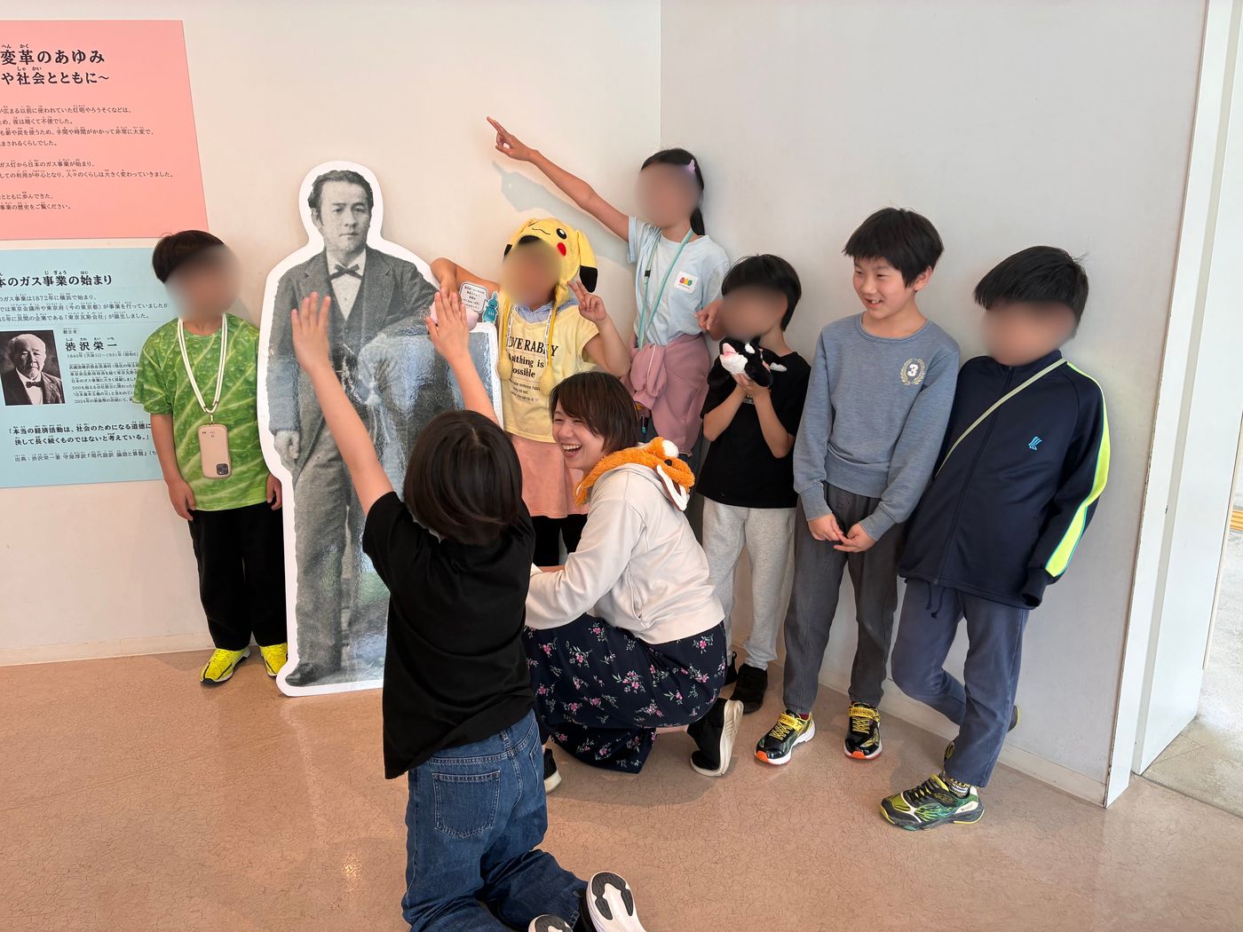 ガスの科学館の歴史展示で渋沢栄一の等身大パネルの前に集まるaini schoolの子どもたち