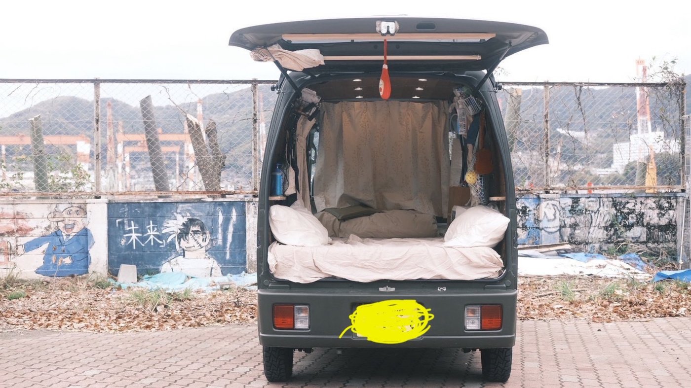 自分で改造した軽トラの荷台に寝床を作り「大工りっきー」と書かれたスライド