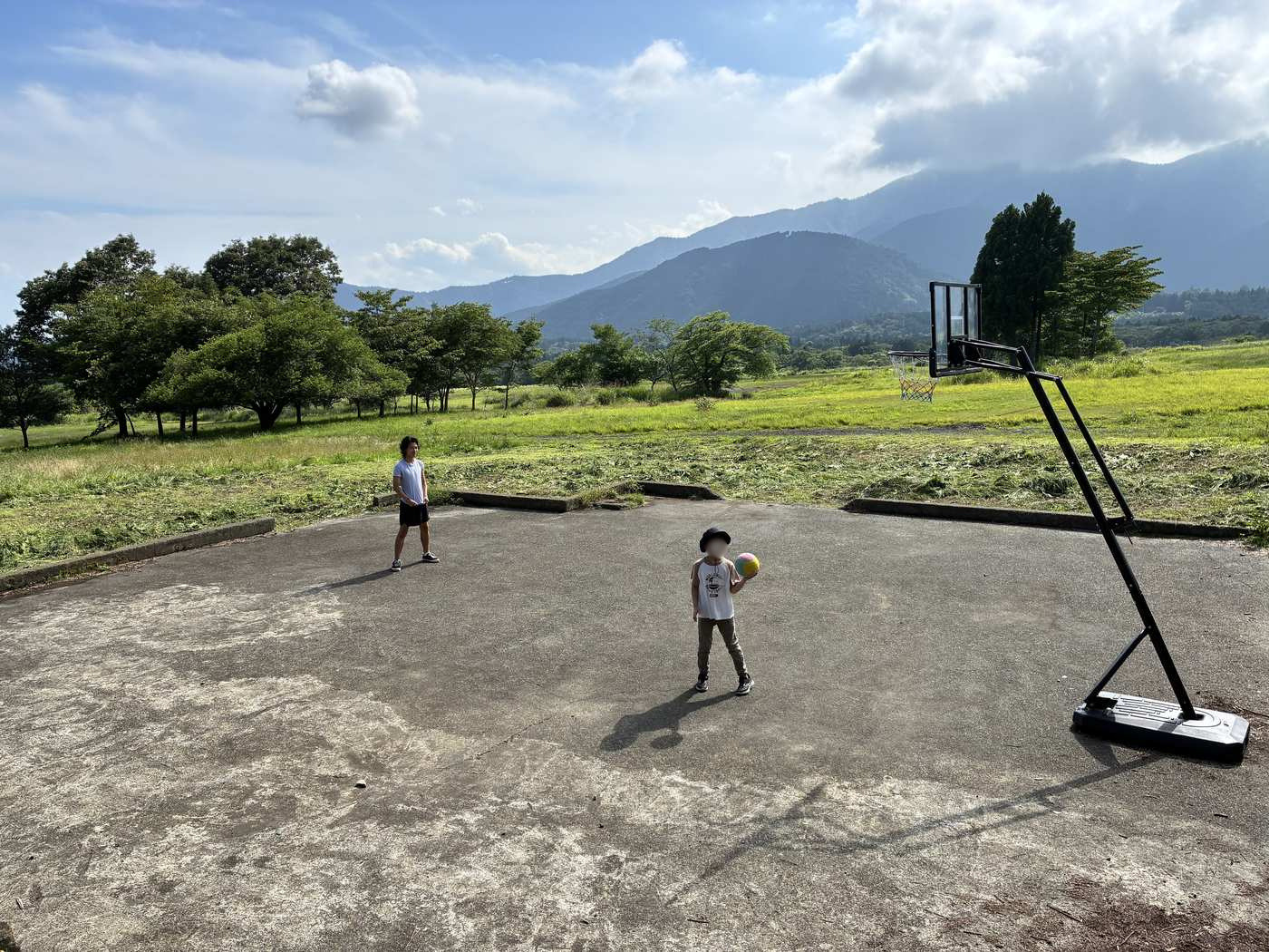 富士山麓の緑豊かな山並みを背景にしたバスケットコートで遊ぶ子どもとスタッフ