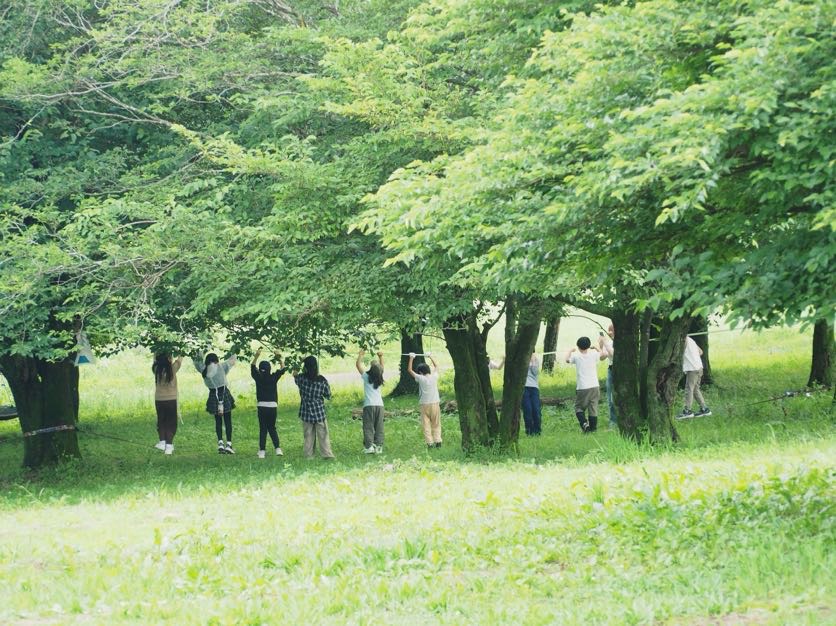 緑豊かな林の中でスラックラインに挑戦するaini schoolの生徒たち、後ろ姿