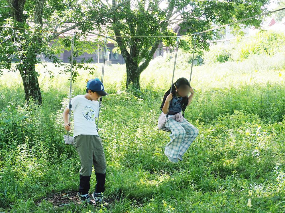 緑豊かな木々の下でブランコを楽しむaini schoolの子どもたち