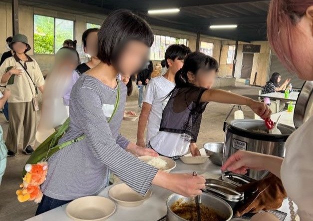カレーの盛り付けをするaini schoolの参加者たち、炊飯器と飯盒が並んでいる