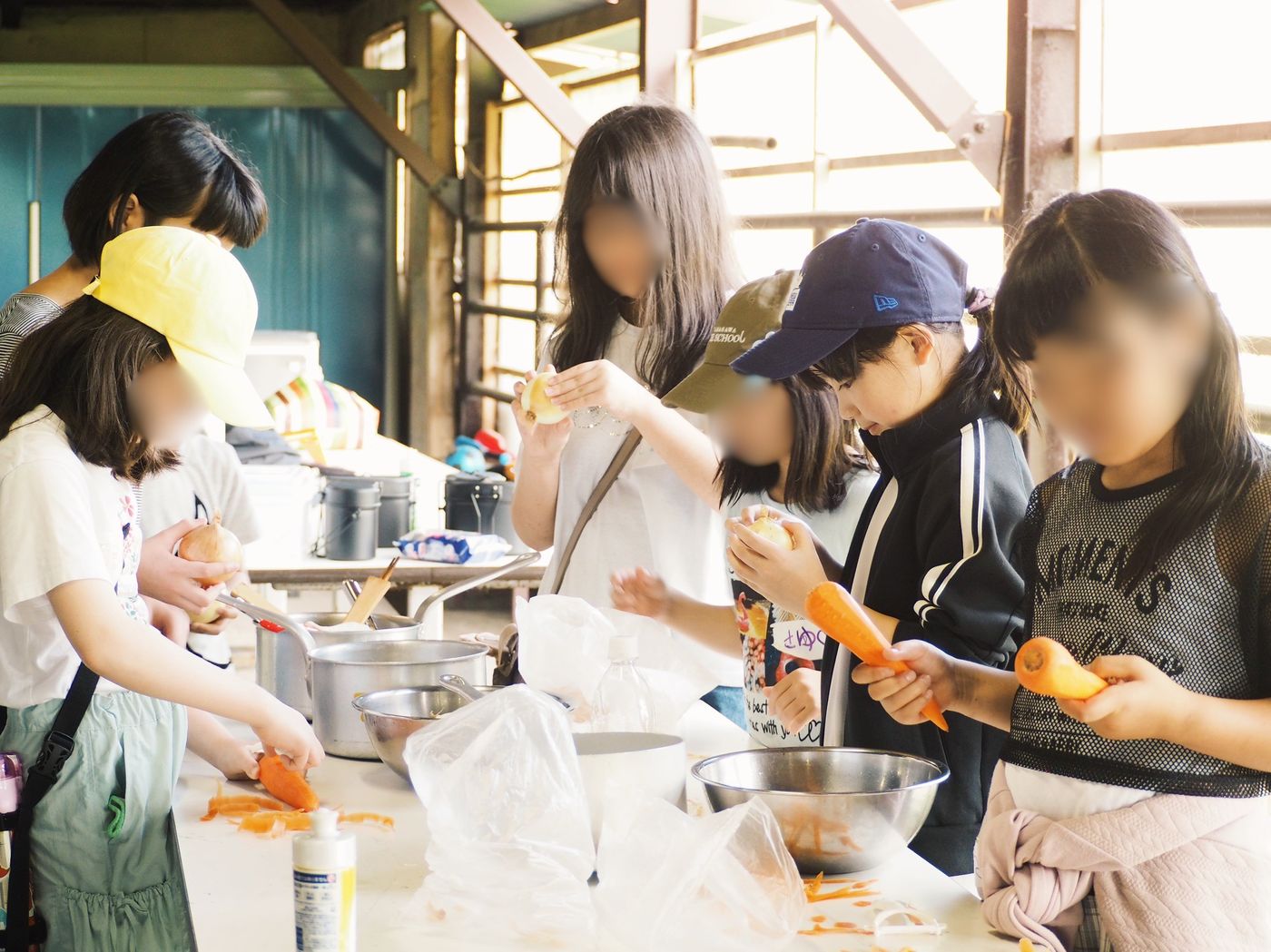 屋外炊事場でにんじんやじゃがいもの皮をむくaini schoolの生徒たち