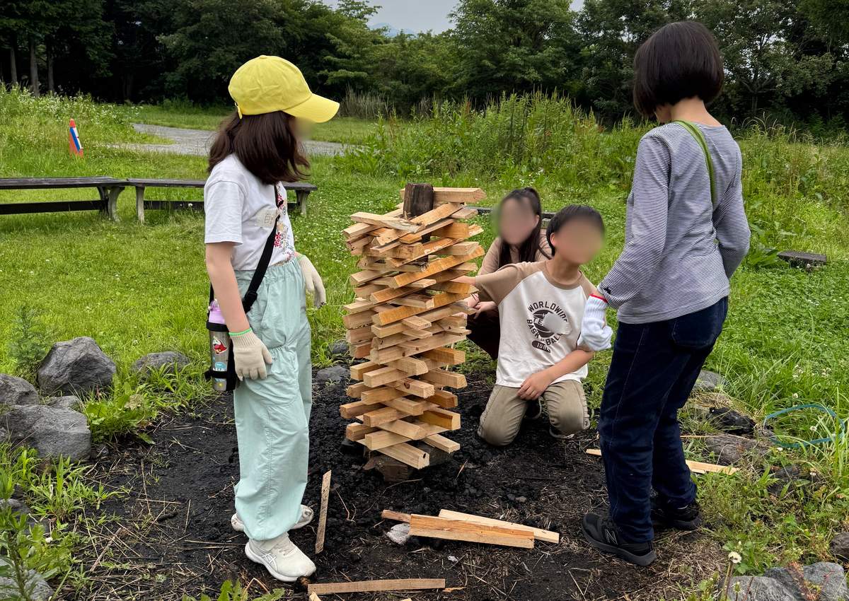 屋外でキャンプファイヤー用に薪を積み上げる準備をするaini schoolの生徒たち