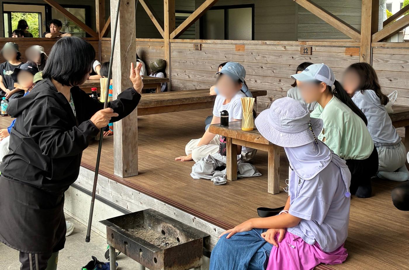 屋外の東屋でスタッフから釣り竿の使い方を説明してもらうaini schoolの生徒たち