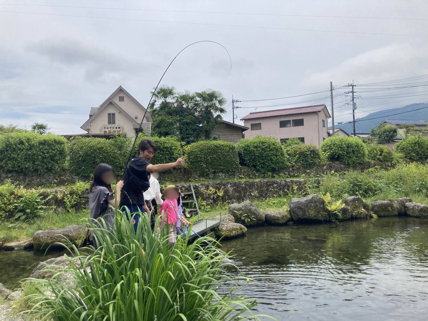 緑豊かな池のほとりでニジマス釣りに挑戦するaini schoolの生徒とスタッフ