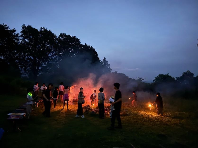 夜空の下、カラフルな煙と花火の光に包まれながら花火を楽しむaini schoolの生徒とスタッフたち