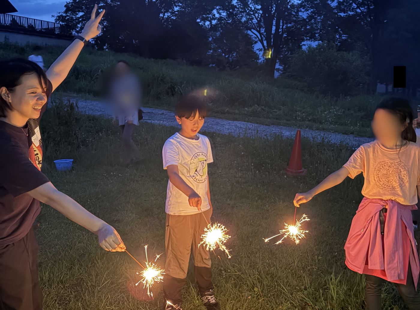 夕暮れの中でスタッフと生徒たちが手持ち花火を楽しむ様子
