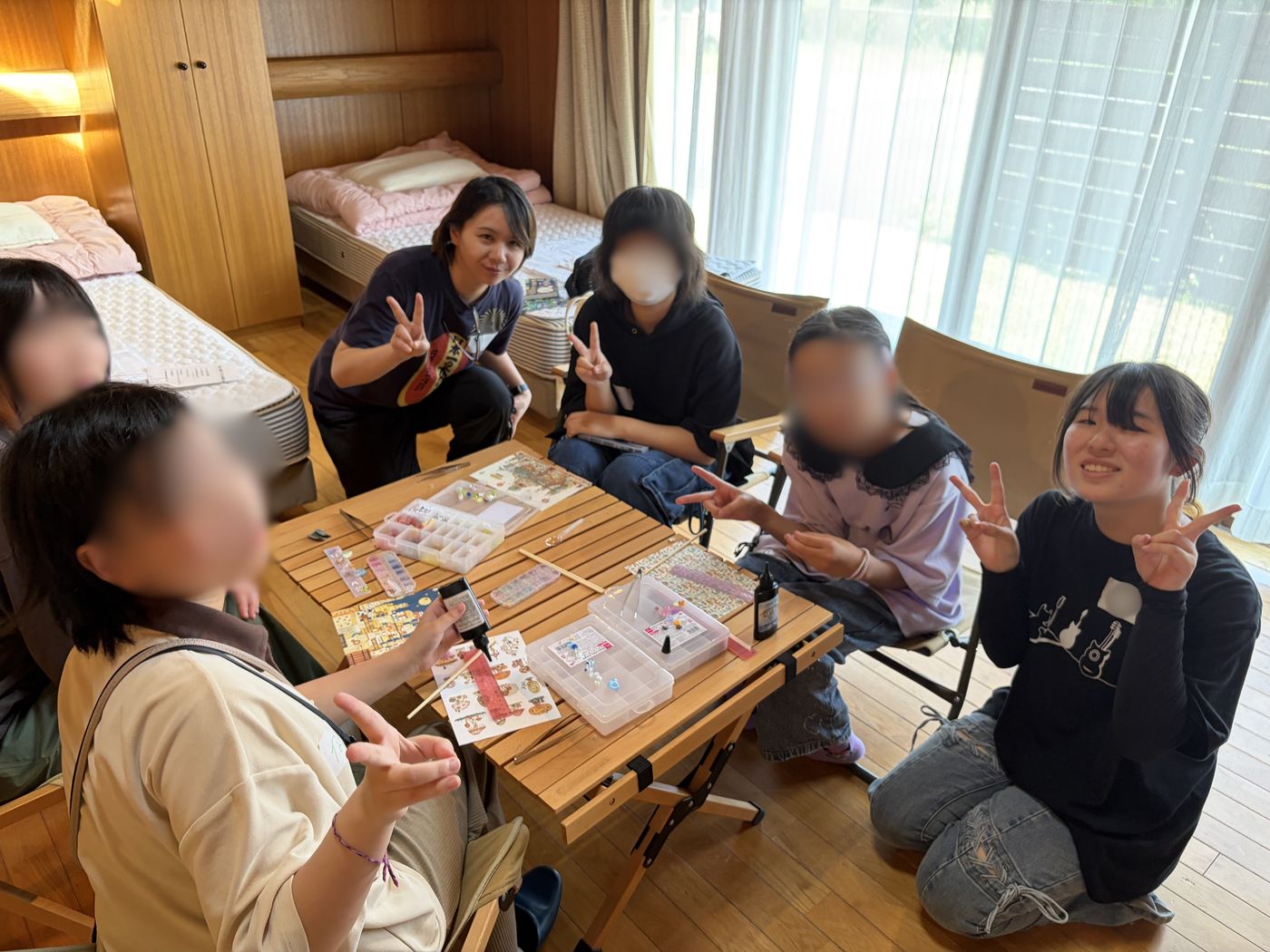 YMCAの宿泊部屋でテーブルを囲み、ビーズやシールなどでハンドメイドを楽しむ生徒とスタッフたち