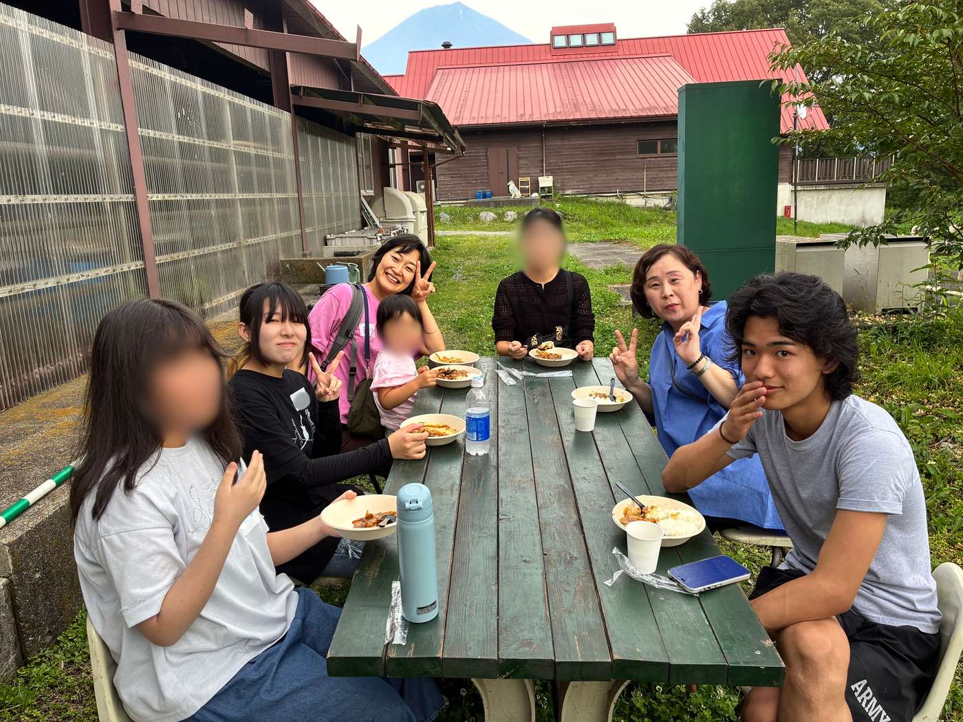富士山YMCAの屋外ピクニックテーブルでカレーを食べる生徒・保護者・スタッフ、背景に富士山