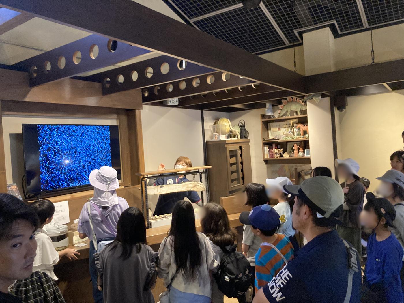 奇石博物館の館内でスクリーンの展示説明に見入るaini schoolの参加者たち