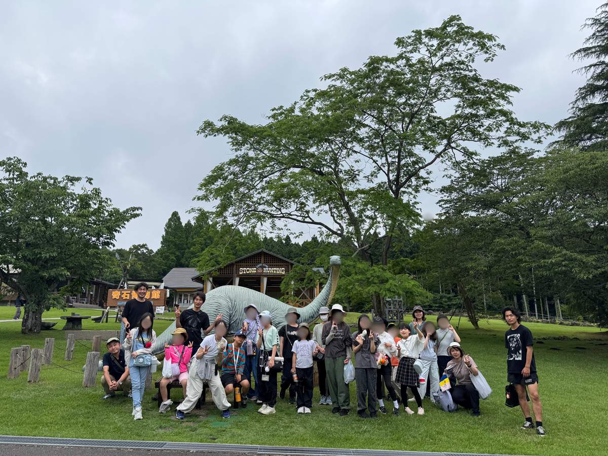 奇石博物館の恐竜モニュメントの前に集まるaini schoolの生徒とスタッフたち