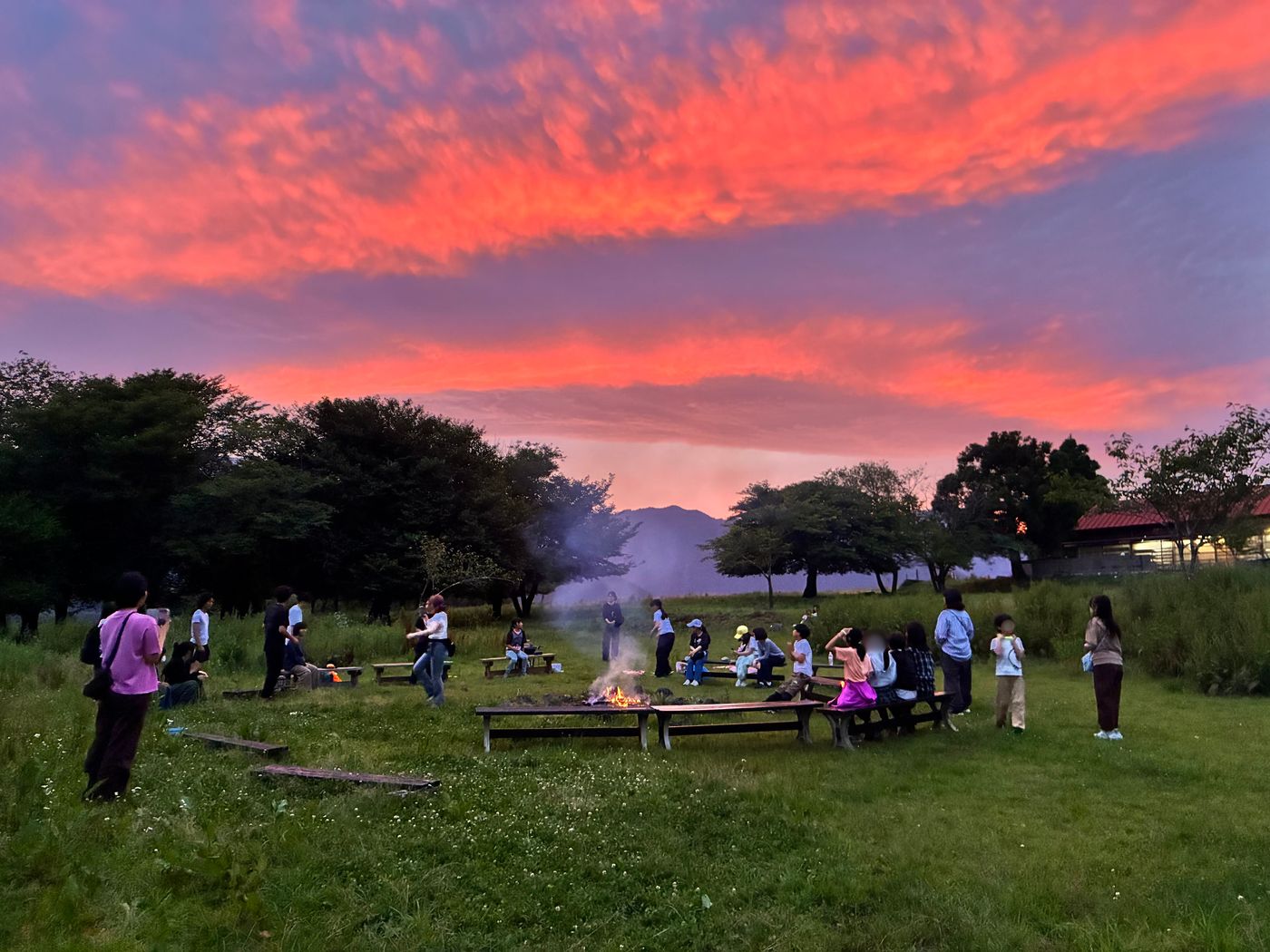 真っ赤な夕焼け空の下、キャンプファイヤーを囲むaini schoolの生徒とスタッフたち