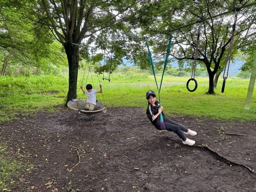 緑の草原に並ぶバスケットブランコと通常ブランコで遊ぶaini schoolの子どもたち