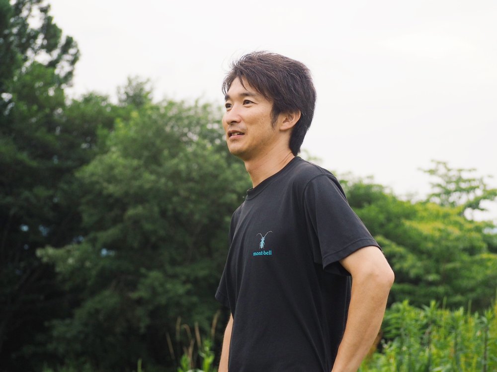 緑を背景に、現地ガイドの田島優介さん（たじまるさん）が笑顔で語りかける様子