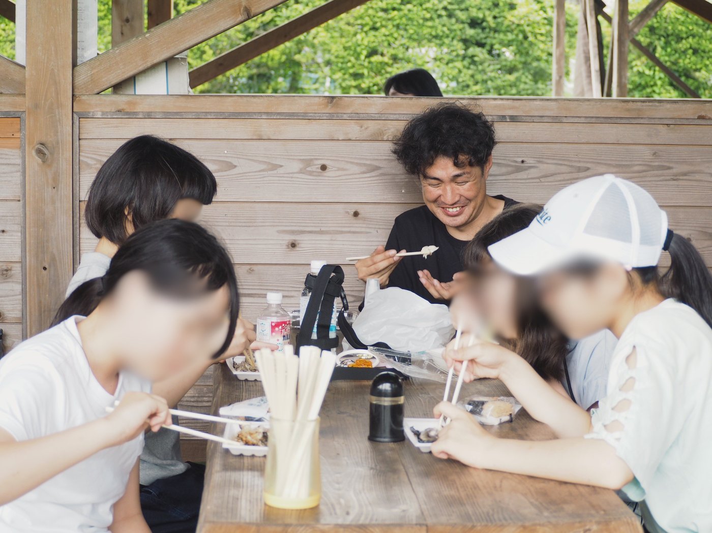 屋外のテーブルで焼きたてのニジマスをスタッフと生徒たちが笑顔で食べる様子